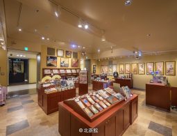 Interior of a modern museum shop in Obuse, displaying Japanese art prints, souvenirs, and books on wooden stands.