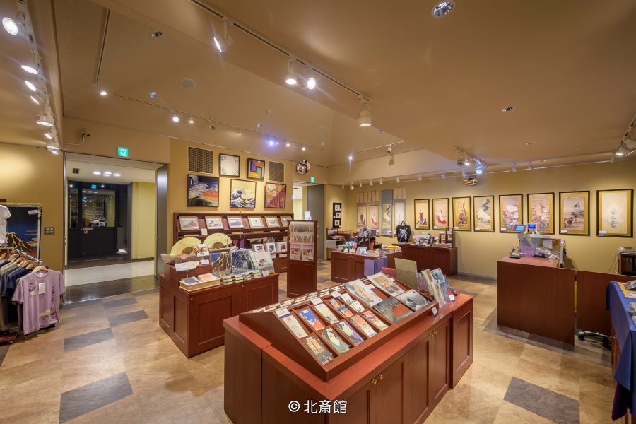 Interior of a modern museum shop in Obuse, displaying Japanese art prints, souvenirs, and books on wooden stands.