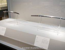 Two Japanese swords (katana) displayed in a brightly lit museum showcase.