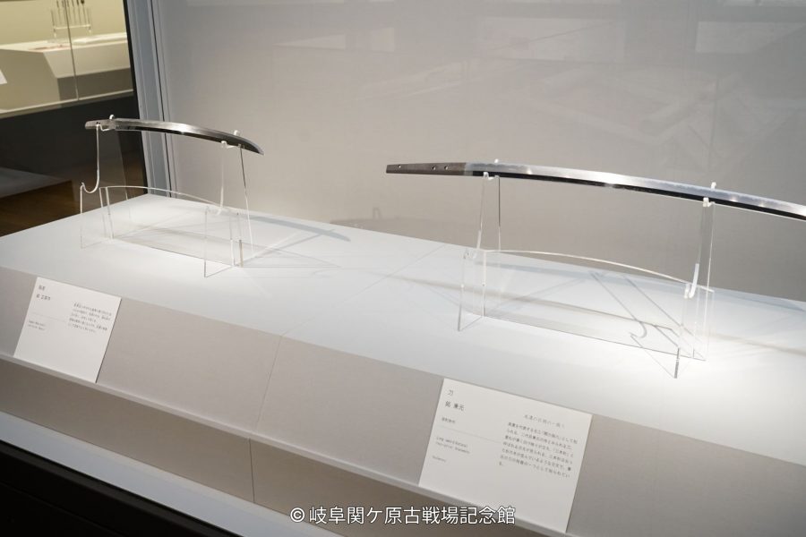 Two Japanese swords (katana) displayed in a brightly lit museum showcase.