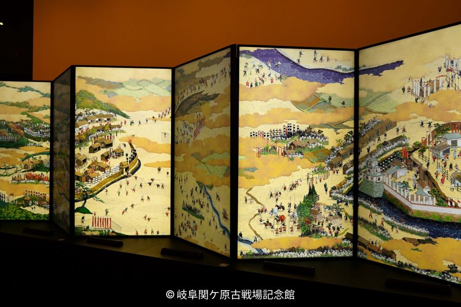 A multi-panel screen painting (byobu) with a detailed depiction of a historic battle or procession on a gold background.