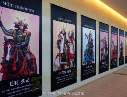A museum hallway lined with large vertical banners displaying portraits of samurai warlords, including Mori Hidemoto and Ukita Hideie.