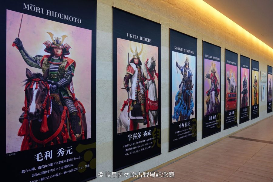 A museum hallway lined with large vertical banners displaying portraits of samurai warlords, including Mori Hidemoto and Ukita Hideie.