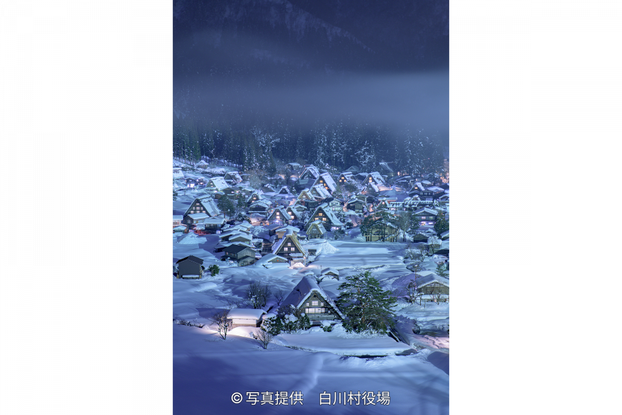 An illuminated Gassho-zukuri village covered in deep snow on a dark winter night.