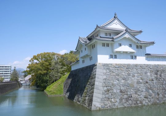 The reconstructed Tatsumi Yagura (turret) of Sunpu Castle standing on the stone wall above the outer moat under a clear blue sky.