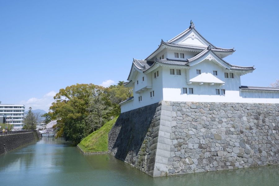 The reconstructed Tatsumi Yagura (turret) of Sunpu Castle standing on the stone wall above the outer moat under a clear blue sky.
