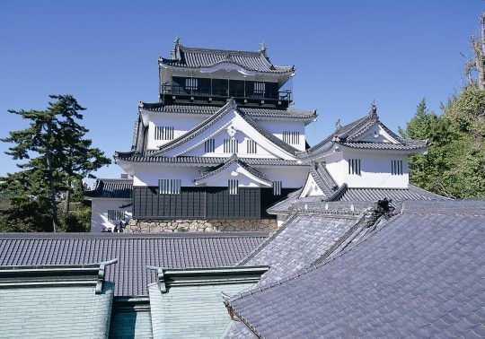 The main keep of the reconstructed Okazaki Castle with white walls and dark tiled roofs, viewed over surrounding rooftops.