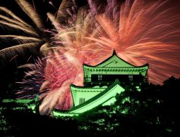 The Okazaki Castle keep illuminated at night against a backdrop of colorful, large fireworks.