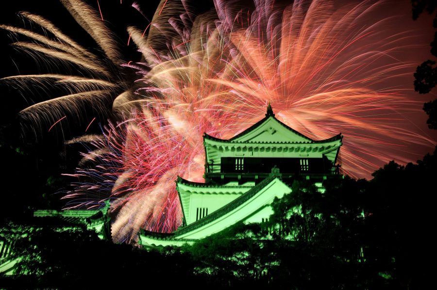 The Okazaki Castle keep illuminated at night against a backdrop of colorful, large fireworks.