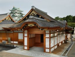 The entrance building of the reconstructed Honmaru Palace, showing intricate eaves and woodwork, with the main castle keep visible in the background.