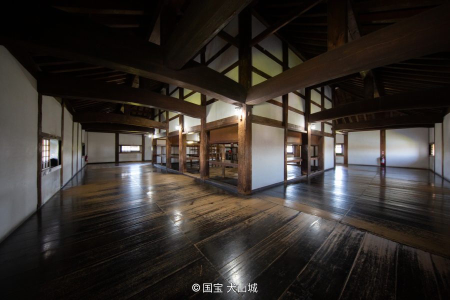 The interior of the Inuyama Castle keep with a wide, dark, polished wooden floor and massive exposed wooden beams.