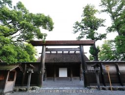 A massive wooden torii gate marking an inner entrance (likely to the Naiku or Geku) of Ise Jingu Shrine, with a traditional fence and thatched roof structure behind it.