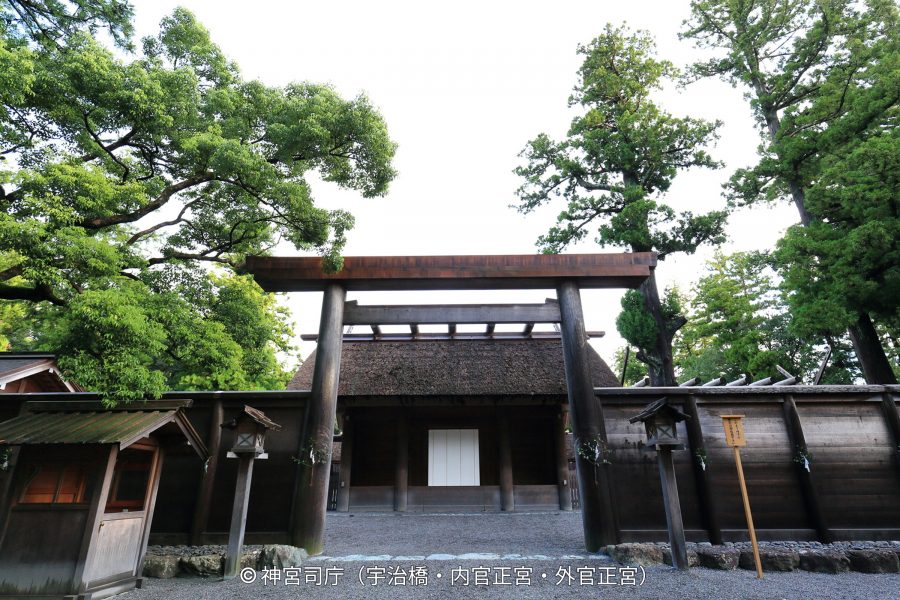 A massive wooden torii gate marking an inner entrance (likely to the Naiku or Geku) of Ise Jingu Shrine, with a traditional fence and thatched roof structure behind it.