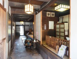 Interior view of a traditional Japanese building with exposed beams, paper lanterns, and a tatami mat area.