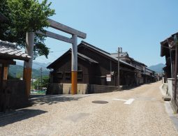 A large wooden torii gate next to a road lined with traditional buildings in Seki-juku under a blue sky.