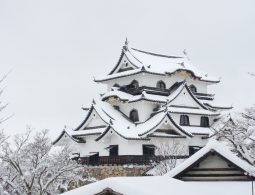 The white-walled main keep of Hikone Castle heavily covered in snow, under a grey sky.