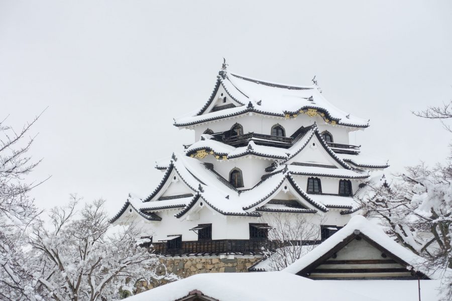 The white-walled main keep of Hikone Castle heavily covered in snow, under a grey sky.