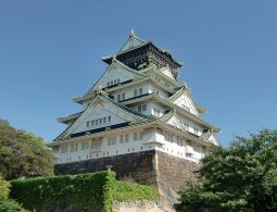 The majestic white and green-tiled main tower of Osaka Castle, sitting atop massive stone walls under a clear blue sky.