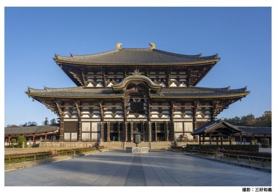 The massive Daibutsuden hall of Todai-ji Temple under a bright blue sky, with a wide, open plaza in the foreground.