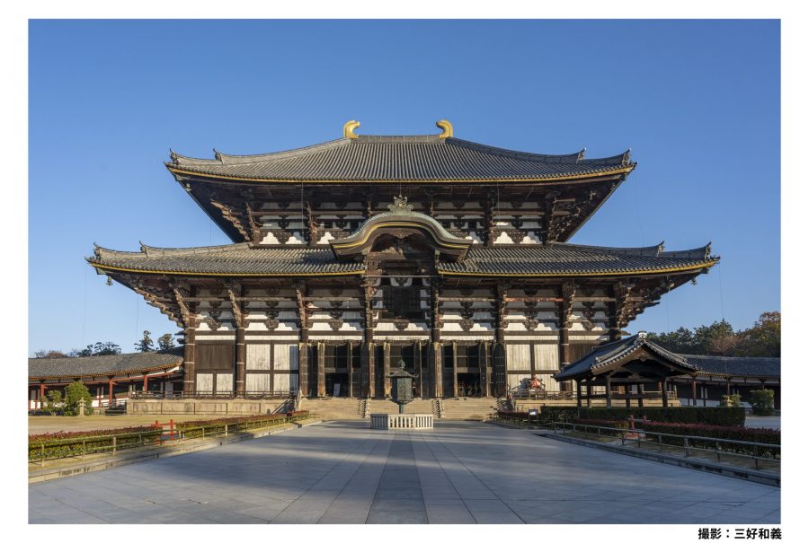 The massive Daibutsuden hall of Todai-ji Temple under a bright blue sky, with a wide, open plaza in the foreground.