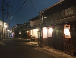 The preserved Naramachi streetscape at dusk, illuminated by warm lights from the traditional wooden houses and hanging lanterns.