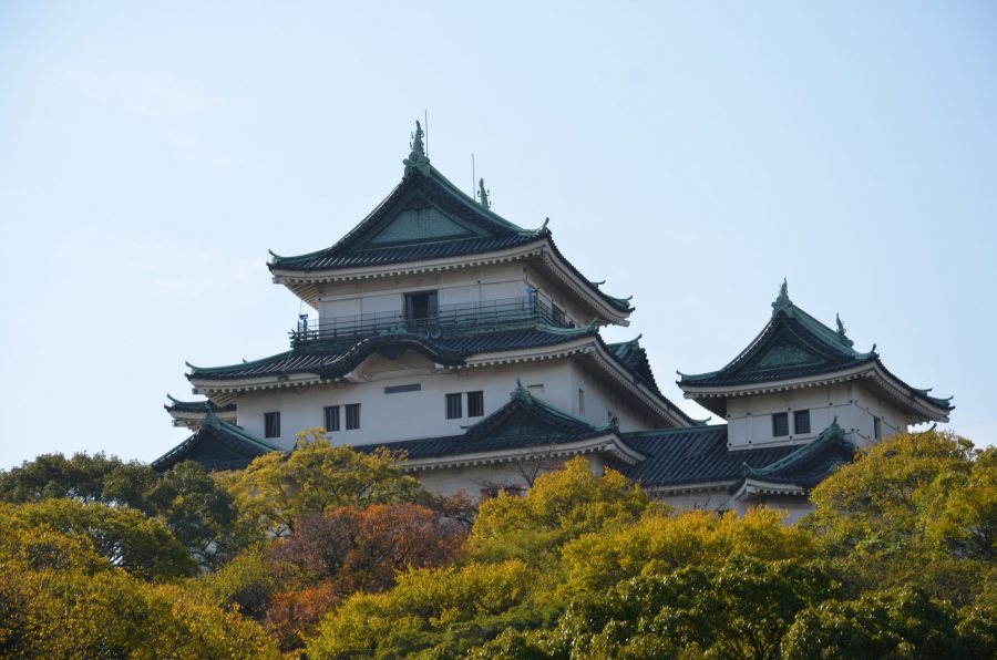Wakayama Castle keep with its green tiled roofs, rising above trees with yellow and orange autumn foliage.