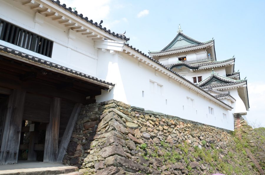 The white castle walls and lower structures of Wakayama Castle, built atop a rough stone foundation.