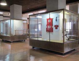 An interior view of the Wakayama Castle museum, showing artifacts like samurai clothing (jinbaori) and weapons displayed in glass cases.