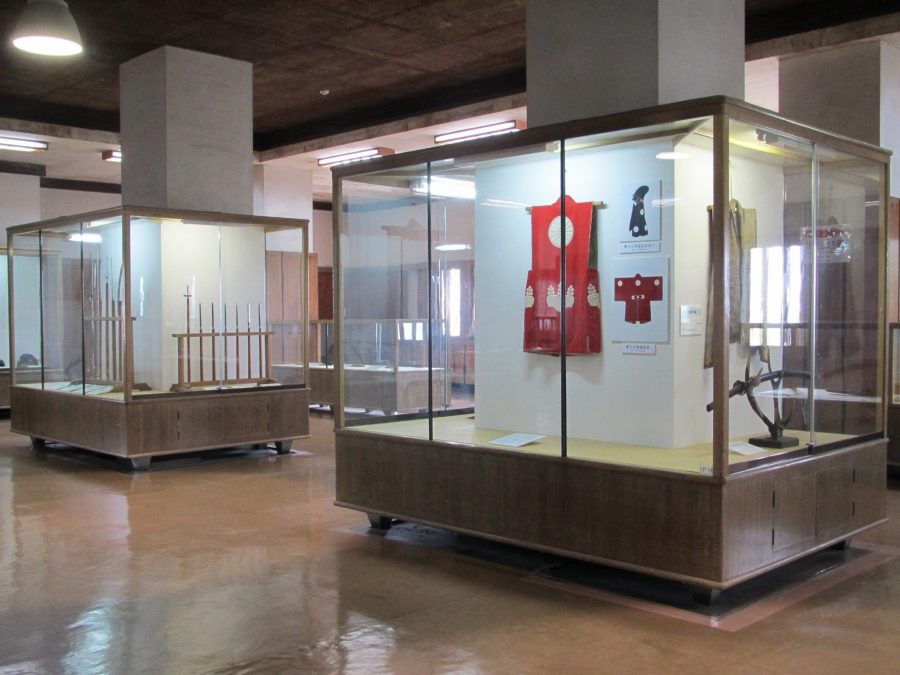 An interior view of the Wakayama Castle museum, showing artifacts like samurai clothing (jinbaori) and weapons displayed in glass cases.