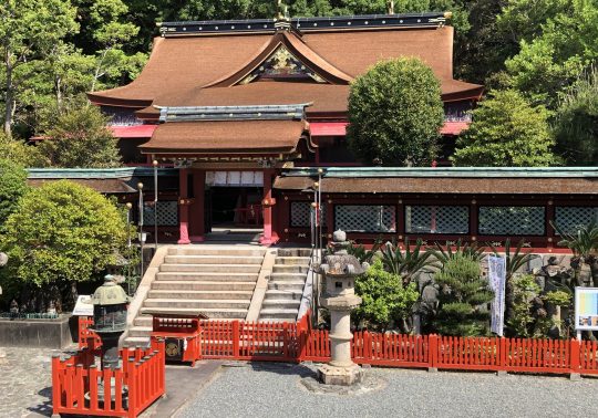 The approach to Kishu Toshogu Shrine, showing the richly colored, ornate temple building behind a red fence and stone lanterns.