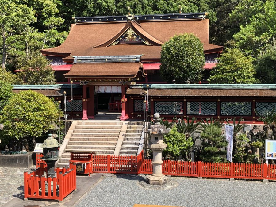 The approach to Kishu Toshogu Shrine, showing the richly colored, ornate temple building behind a red fence and stone lanterns.