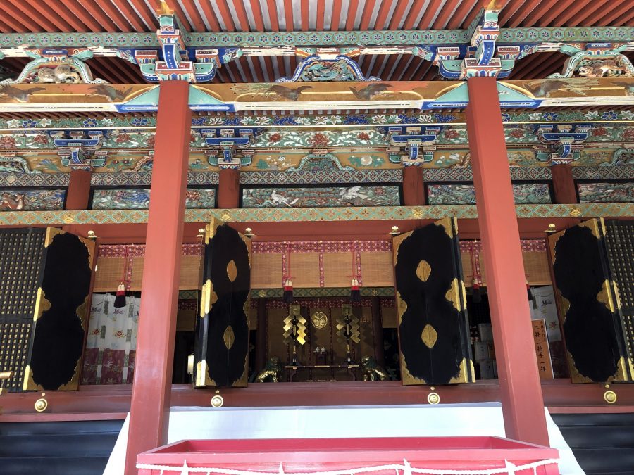 Interior of the Kishu Toshogu Shrine Haiden (Worship Hall), showing detailed, colorful carvings on the ceiling beams and four large black panels with gold accents.