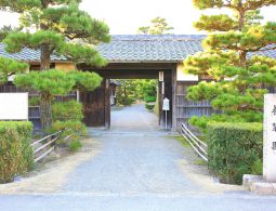 The main entrance gate to Yosuien Garden, flanked by manicured pine trees and a stone monument.