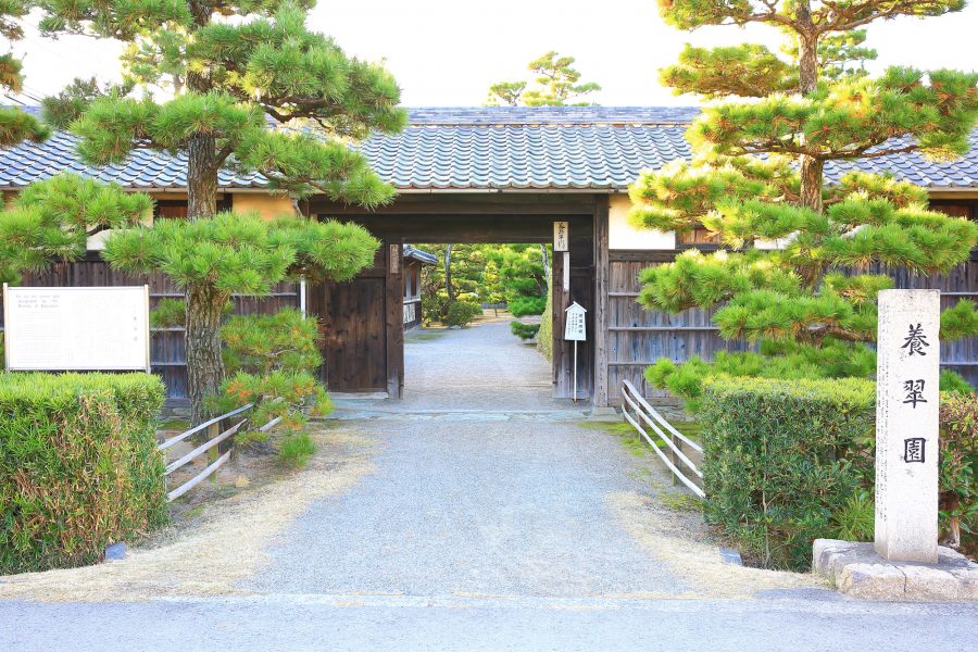 The main entrance gate to Yosuien Garden, flanked by manicured pine trees and a stone monument.