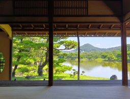View of the Yosuien Garden pond and manicured pine trees from inside a traditional wooden building's veranda.