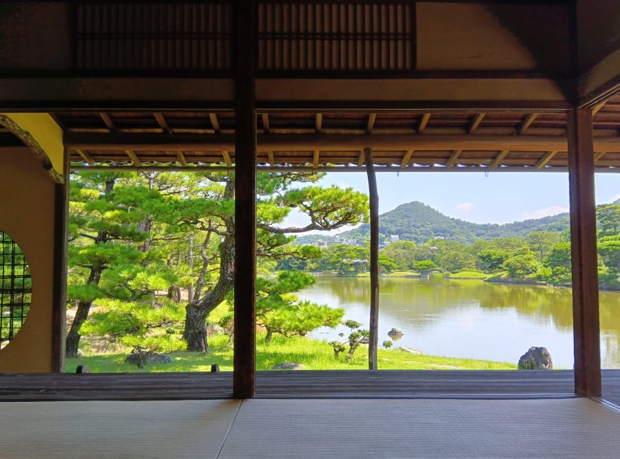 View of the Yosuien Garden pond and manicured pine trees from inside a traditional wooden building's veranda.