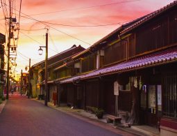 The Kurayoshi white-walled district streetscape at dusk, illuminated by warm lights under a dramatically orange-red sky.