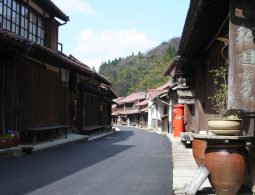 A narrow street in the preserved Omori townscape lined with traditional dark wood merchant houses and an old red mailbox.
