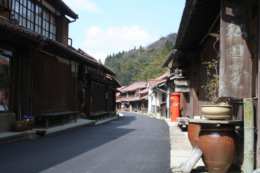 A narrow street in the preserved Omori townscape lined with traditional dark wood merchant houses and an old red mailbox.