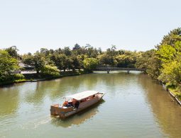 A sightseeing boat on the moat surrounding Matsue Castle, with the castle keep visible in the distance above the trees.
