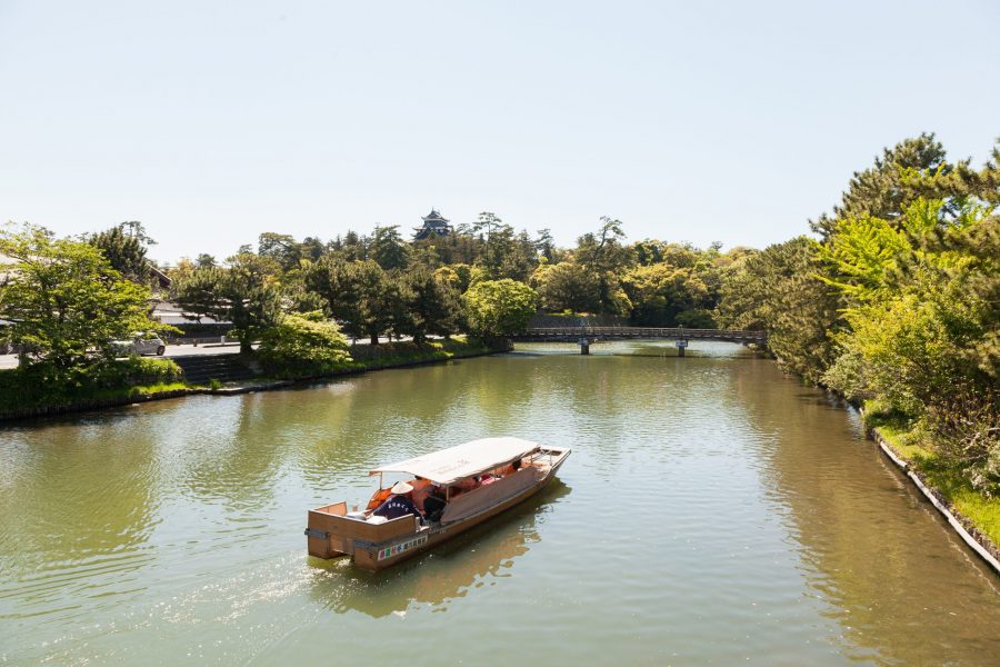 A sightseeing boat on the moat surrounding Matsue Castle, with the castle keep visible in the distance above the trees.
