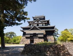 The black and white main keep of Matsue Castle, one of Japan's original castles, standing on its massive stone foundation surrounded by parkland.
