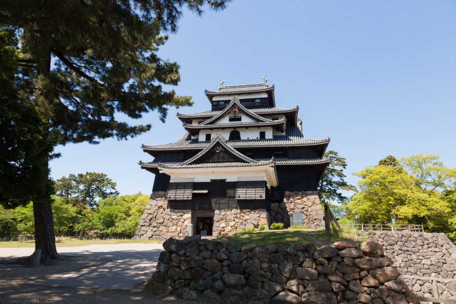 The black and white main keep of Matsue Castle, one of Japan's original castles, standing on its massive stone foundation surrounded by parkland.