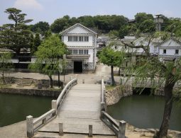 An elevated view over a stone bridge of the white-walled Kurashiki Bikan Historical Area, with a two-story building ahead.