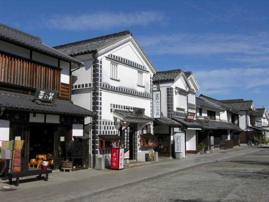 Close-up of the traditional storefronts in the Kurashiki Bikan Historical Area, featuring white walls and black grid-patterned (namako-kabe) gables.