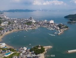 Aerial view of the horseshoe-shaped Tomonoura port town and harbor, surrounded by forested hills and the Seto Inland Sea.