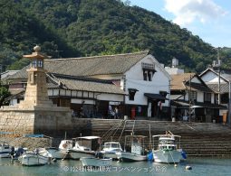 Fishing boats moored in the Tomonoura harbor in front of the historic stone Joyato (all-night lighthouse) and preserved Edo-period buildings.