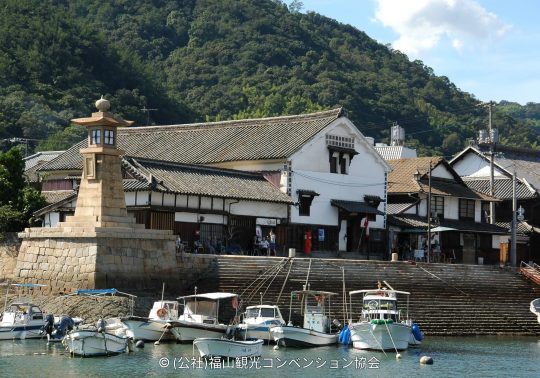 Fishing boats moored in the Tomonoura harbor in front of the historic stone Joyato (all-night lighthouse) and preserved Edo-period buildings.