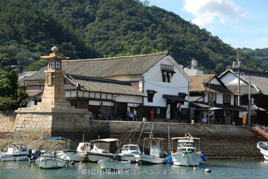 Fishing boats moored in the Tomonoura harbor in front of the historic stone Joyato (all-night lighthouse) and preserved Edo-period buildings.