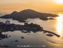 Aerial view of the Tomonoura harbor and the surrounding landmass silhouetted against a brilliant sunset over the Seto Inland Sea.